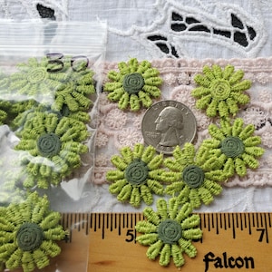 May include: A collection of green embroidered flower appliques with dark green centers. Some are in a clear plastic bag with the number "30" written on it. A quarter coin and a wooden ruler are also in the image.