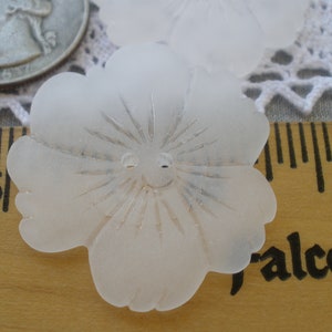May include: A white frosted glass flower button with a raised center and a smiley face design. The button is approximately 1 inch in diameter.