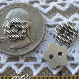 May include: Three silver metal flower-shaped buttons with two holes each. The buttons are about the size of a US quarter.