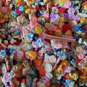 May include: A close-up of a silver spoon with a cluster of colorful fabric flowers on the end. The flowers are made of various shades of pink, blue, yellow, and green.