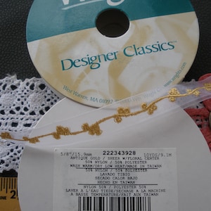 May include: Two spools of Wrights Designer Classics ribbon. One spool is teal and white, the other is white. The white ribbon has a gold floral design. The label reads "Antique Gold / Sheer w/Floral Center".