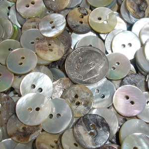 May include: A collection of round, two-hole buttons in various shades of white, brown, and iridescent colors. A US dime is included for size reference. The buttons have a pearlescent sheen and are likely made of mother of pearl.