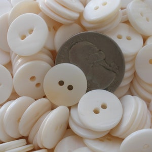 May include: A large pile of white, round, two-hole buttons. The buttons are approximately the size of a US quarter.