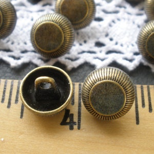 May include: A close-up of two antique gold-toned buttons with a raised rim and a flat center. The buttons have a shank on the back for sewing.