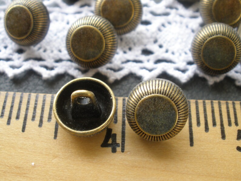 May include: A close-up of two antique gold-toned buttons with a raised rim and a flat center. The buttons have a shank on the back for sewing.
