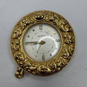 May include: A vintage Seth Thomas clock with a gold-coloured, ornate, circular frame. The clock face is white with gold-coloured hour markers and hands. The clock has a small, decorative base. The clock face reads "Seth Thomas".