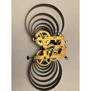 May include: A vintage clock mechanism with brass gears and a metal frame. The clock's internal workings are visible, including the intricate gear system. The design includes curved metal bands on either side, creating a unique, abstract shape.