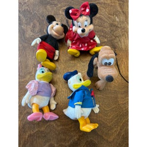 Peut inclure: Un ensemble de cinq figurines Disney floquées comprenant Mickey Mouse en short rouge, Minnie Mouse en robe rouge à pois, Daisy Duck avec un haut violet, Donald Duck en tenue de marin bleu et Pluto avec une fourrure beige et des oreilles noires.