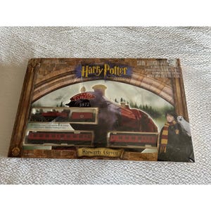 May include: A boxed Harry Potter Hogwarts Express train set. The packaging features the Hogwarts Express train, a scenic background, and images of Harry Potter and Hedwig. The set includes a train engine, tender, and passenger cars.