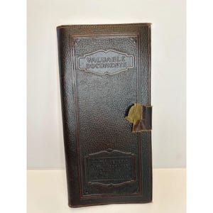 May include: A dark brown, textured leather document holder featuring the embossed text VALUABLE DOCUMENTS at the top. The rectangular case includes a central vertical panel with decorative borders and a worn, light-colored tab closure on the right side.