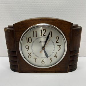 May include: A vintage Sessions clock with a wooden frame and a silver-toned clock face. The clock face features black numerals and hands, with the word "Sessions" printed on the face. The clock is made in the U.S.A.