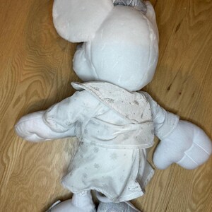Puede incluir: Mu&ntilde;eca de peluche blanca de Minnie Mouse con lazo, vestido y zapatos plateados. El vestido tiene un estampado de copos de nieve. Se ven las orejas y las manos grandes de la mu&ntilde;eca. La mu&ntilde;eca mide unos 30 cm de alto.