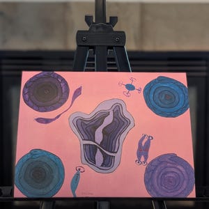 May include: Abstract painting on a canvas, featuring a pink background with various shapes in shades of blue, purple, and gray. The artwork is displayed on a black easel, with a fireplace visible in the background.