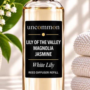 May include: A clear glass bottle filled with light amber liquid, featuring a black rectangular label with the text uncommon, LILY OF THE VALLEY, MAGNOLIA, JASMINE, White Lily, and REED DIFFUSER REFILL. The bottle has a silver metallic cap.
