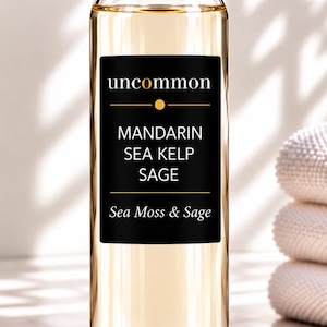 May include: A clear glass bottle filled with a light amber liquid, featuring a black rectangular label with white text that reads uncommon, MANDARIN, SEA KELP, SAGE, and Sea Moss & Sage, topped with a metallic silver cylindrical cap.
