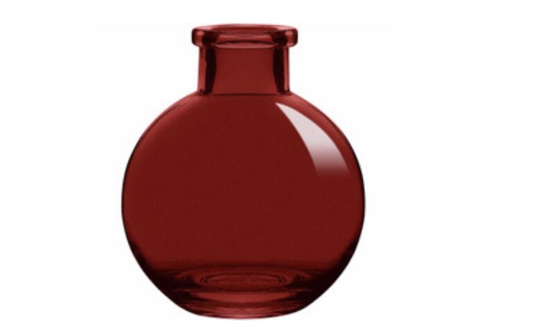 Pu&ograve; includere: Un piccolo vaso sferico in vetro di un colore rosso bordeaux profondo e traslucido. Il recipiente presenta un corpo liscio e arrotondato che si restringe in un collo cilindrico corto con un bordo spesso e arrotondato sulla parte superiore, creando una silhouette semplice.
