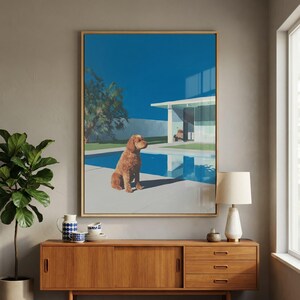 May include: Art print depicting a brown dog by a blue swimming pool. The artwork has a mid-century modern style, with a clear blue sky and a white modernist house in the background. The print is displayed above a wooden cabinet, with a lamp and plant.