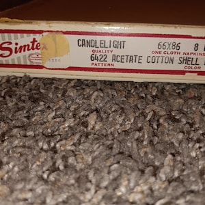 May include: A box of Simtex Candlelight 6422 acetate cotton napkins in shell pink. The box is labeled with the size 66x86 and 8 18x18.