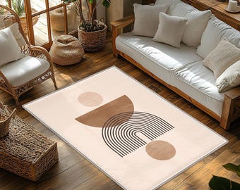 May include: A rectangular area rug featuring a cream-colored background with a central graphic design. The pattern consists of a solid brown semicircle, a series of thin black concentric arches, and two solid light brown circles.