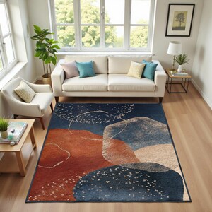 May include: A rectangular area rug with an abstract design. The rug features a dark blue background with large, overlapping shapes in shades of rust, beige, and blue. White dotted lines and accents add detail. The rug is placed in a living room setting.