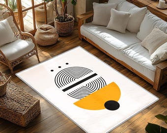May include: A rectangular area rug featuring a white background with a graphic design consisting of black concentric semi-circles, a solid horizontal black bar, a large yellow semi-circle, and a solid black circle positioned at the bottom.