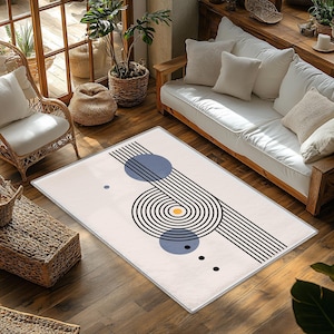 Peut inclure: Un tapis rectangulaire avec un fond crème et un motif géométrique. Le motif présente des lignes noires, des cercles bleus et un cercle jaune. Le tapis est posé sur un sol en bois dans un salon.