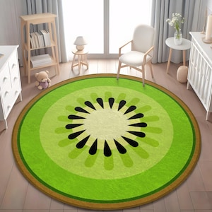 May include: A round rug with a kiwi fruit design. The rug features concentric circles of green hues, with a brown border and black seed details in the center. The rug is placed on a wooden floor.