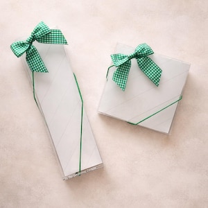 May include: Two clear gift boxes with white diagonal stripes and green gingham bows. One box is rectangular, the other square. Both are tied with green string. The text "The Occasional Cookie" is visible on the rectangular box.