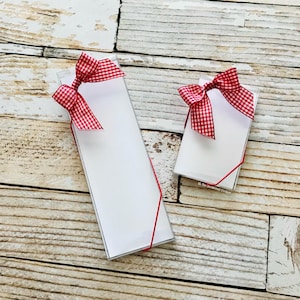 May include: Two clear boxes with white note cards inside. Each box is tied with a red and white gingham ribbon.