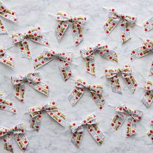 May include: Multiple white bows with a school-themed ribbon featuring red apples and yellow school buses. The bows are arranged on a light gray surface, perfect for crafting or gift wrapping.