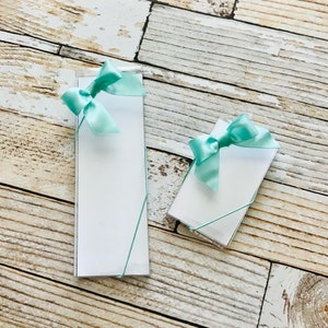 May include: Two sets of blank note cards with aqua blue ribbon bows. The note cards are packaged in clear plastic boxes.
