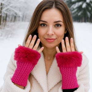 May include: Bright pink fingerless gloves with a knitted design and a fluffy, fuchsia fur trim. The gloves are worn with a white coat against a snowy, winter backdrop. A stylish accessory for cold weather.