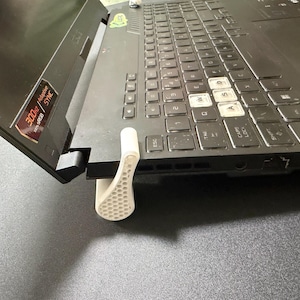 May include: A black laptop with a white and grey keyboard. A white, honeycomb-patterned support prop is attached to the laptop. The screen displays text, including "300Hz" and "Adaptive Sync".