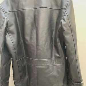 May include: A black leather jacket with a faux fur collar. The jacket features a classic design with a button closure, two front pockets, and adjustable cuffs with buckles. The back of the jacket has a tailored fit with vertical seams.