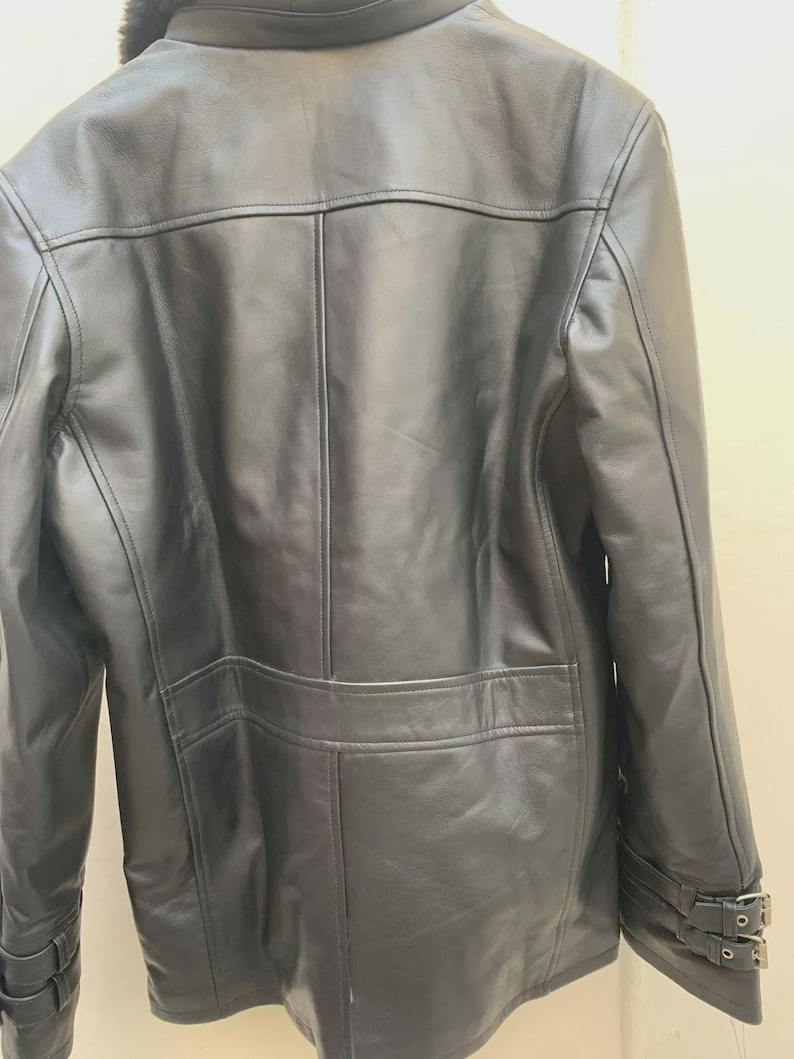May include: A black leather jacket with a faux fur collar. The jacket features a classic design with a button closure, two front pockets, and adjustable cuffs with buckles. The back of the jacket has a tailored fit with vertical seams.