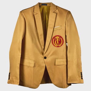 Könnte beinhalten: Senfgelber Blazer mit Ein-Knopf-Verschluss und einem rot-goldenen Emblem auf der Brust. Der Blazer hat ein fallendes Revers, eine Brusttasche und zwei Vordertaschen. Die Ärmel haben vier Knöpfe.