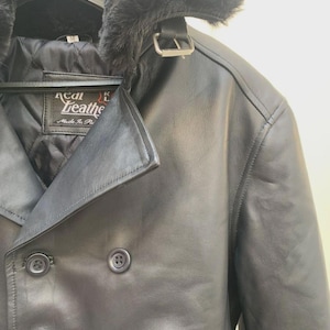 May include: Black leather jacket with a faux fur collar and a double-breasted design. The jacket features a buckle closure at the collar and button closures down the front. The label reads "Real Leather Made in Italy".