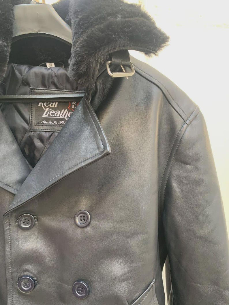 May include: Black leather jacket with a faux fur collar and a double-breasted design. The jacket features a buckle closure at the collar and button closures down the front. The label reads "Real Leather Made in Italy".