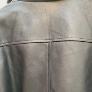 May include: Close-up of a black leather jacket's back, showcasing the collar, shoulder yoke, and vertical seam. The jacket features a shearling collar and detailed stitching, highlighting its craftsmanship. The leather appears smooth and supple.