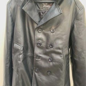 May include: A black leather coat with a double-breasted design. The coat features a notched collar, a faux fur trim, and multiple buttons. The coat has a label that reads "Real Leather".