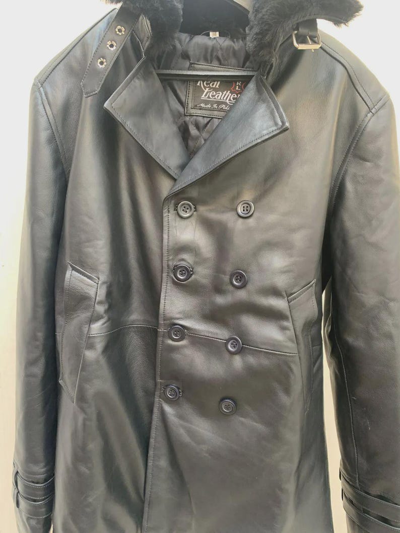 May include: A black leather coat with a double-breasted design. The coat features a notched collar, a faux fur trim, and multiple buttons. The coat has a label that reads "Real Leather".