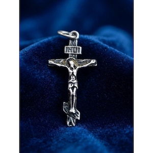 Könnte beinhalten: Ein silberfarbener Metall-Kruzifix-Anhänger mit einer detaillierten Darstellung von Jesus am Kreuz. Das Design umfasst einen oberen Querbalken, einen mittleren Querbalken und eine schräge Fußstütze unten. Die Buchstaben INRI sind oben eingraviert.