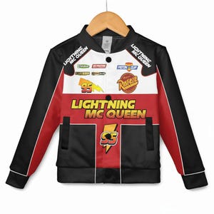 May include: A Lightning McQueen bomber jacket in black, red, and white. The jacket features the text "Lightning McQueen" and "95" with various logos and patches. The sleeves are black with red accents, and the jacket is hanging on a wooden hanger.