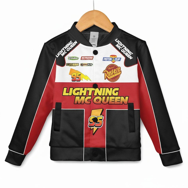 May include: A Lightning McQueen bomber jacket in black, red, and white. The jacket features the text "Lightning McQueen" and "95" with various logos and patches. The sleeves are black with red accents, and the jacket is hanging on a wooden hanger.