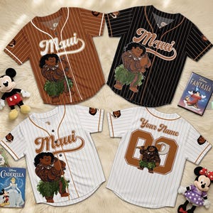 K&ouml;nnte beinhalten: Vier Baseball-Trikots mit dem Wort "Maui" und einer Cartoon-Figur. Zwei sind braun mit wei&szlig;en Nadelstreifen, eines ist schwarz mit wei&szlig;en Nadelstreifen und eines ist wei&szlig; mit braunen Nadelstreifen. Auf dem R&uuml;cken eines Trikots steht "Your Name" und eine Nummer.