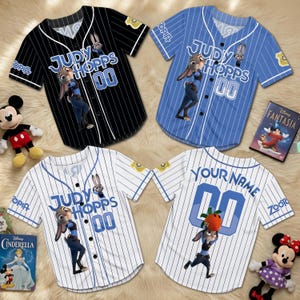 Puede incluir: Cuatro camisetas de b&eacute;isbol a rayas con el personaje Judy Hopps de Zootopia. Las camisetas son negras, azules y blancas. Cada camiseta tiene el nombre "JUDY HOPPS" y el n&uacute;mero "00" en la parte delantera. Una camiseta tiene "YOUR NAME" en la espalda.
