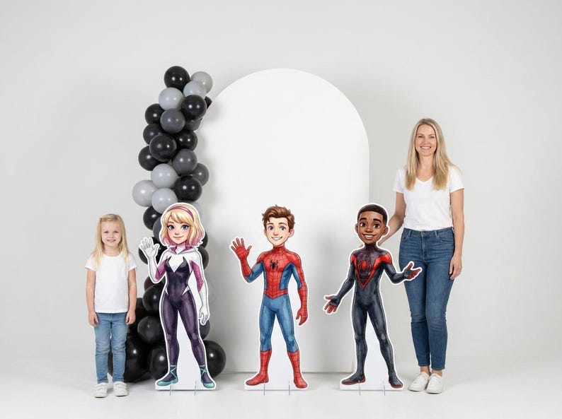 May include: A group of three superhero character cutouts, including Spider-Man, Spider-Gwen, and Miles Morales, stand in front of a white backdrop. A young girl and an adult woman are also in the image. A black and gray balloon arch is on the left.
