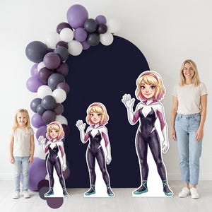 May include: A party scene featuring three cardboard cutouts of a female superhero in a black and white suit, with a blonde bob and a pink headband. A balloon arch in shades of purple, gray, and white is on the left.
