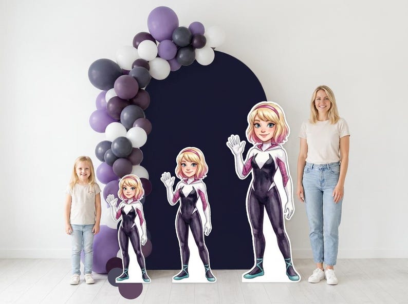 May include: A party scene featuring three cardboard cutouts of a female superhero in a black and white suit, with a blonde bob and a pink headband. A balloon arch in shades of purple, gray, and white is on the left.