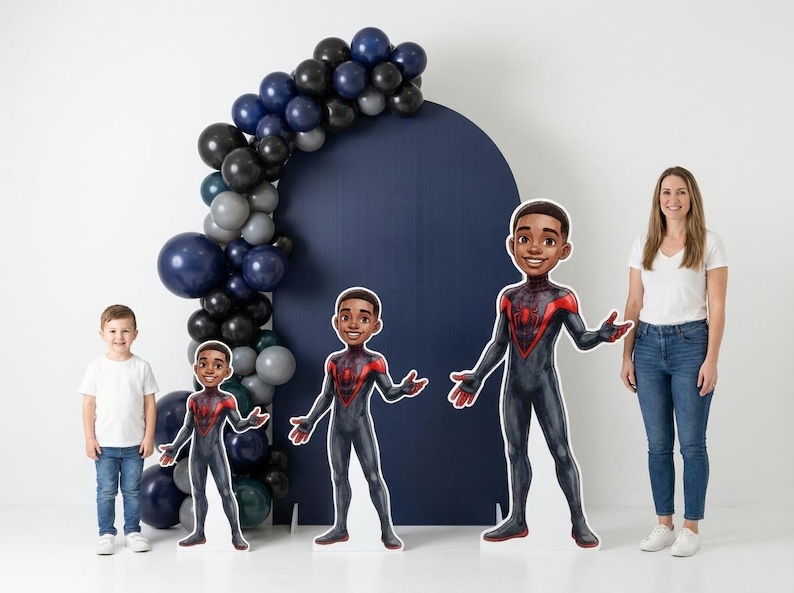 May include: A party scene with a navy blue backdrop, a balloon arch, and three cardboard cutouts of a superhero. A woman and a young boy are also in the image. The balloons are in shades of blue, gray, and black.